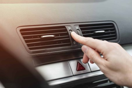 Finger adjusting air outlet deflector of HVAC on dashboard in car.