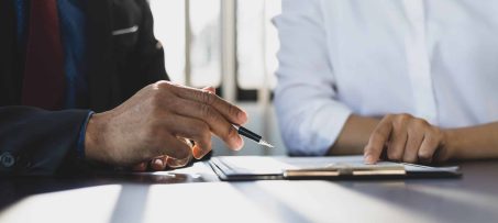 Businessman in suit in his office showing an insurance policy and pointing with a pen where the policyholder must to sign. Insurance agent presentation and consulting insurance detail to customer.