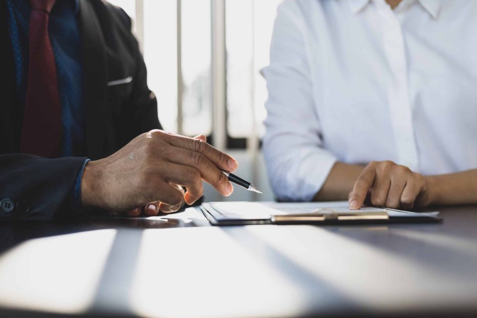 Businessman in suit in his office showing an insurance policy and pointing with a pen where the policyholder must to sign. Insurance agent presentation and consulting insurance detail to customer.