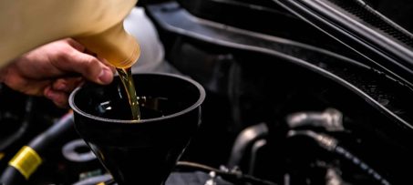 Close up of male hands adding oil with a funnel after a do-it-yourself oil change. Selective focus