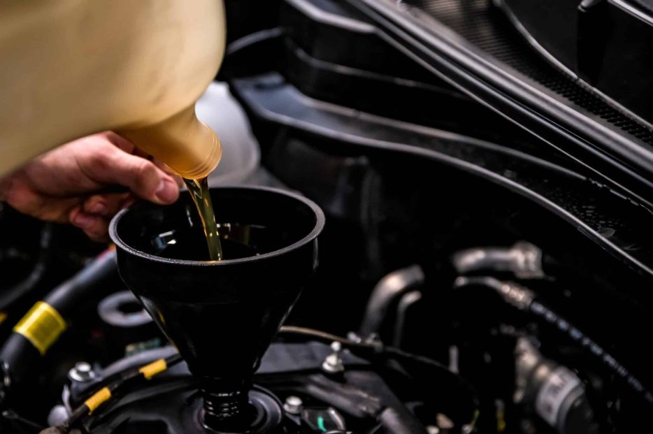 Close up of male hands adding oil with a funnel after a do-it-yourself oil change. Selective focus
