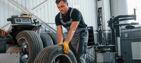 Walking with tyre. Man in uniform is working in the auto service.