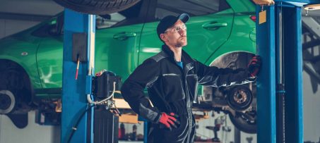 Car Mechanic and the Auto Service Center. Automotive Industry. Caucasian Worker Between Car Lifts.