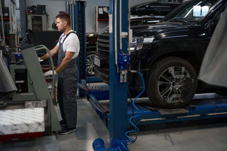 Worker in special suit, protective gloves standing near computer and checking car wheel in garage