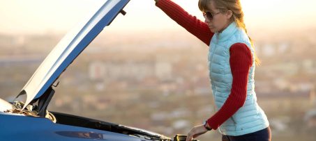 Young woman opening bonnet of broken down car having trouble with her vehicle. Female driver near auto with popped up hood.